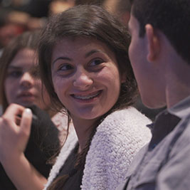 One student smiles at another as they sit with the rest of the audience.