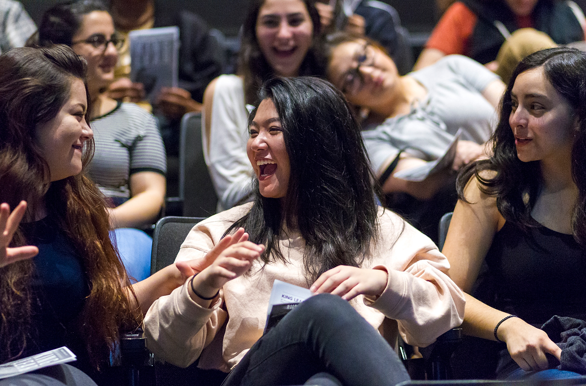 Students laugh with one another as they sit in the audience.